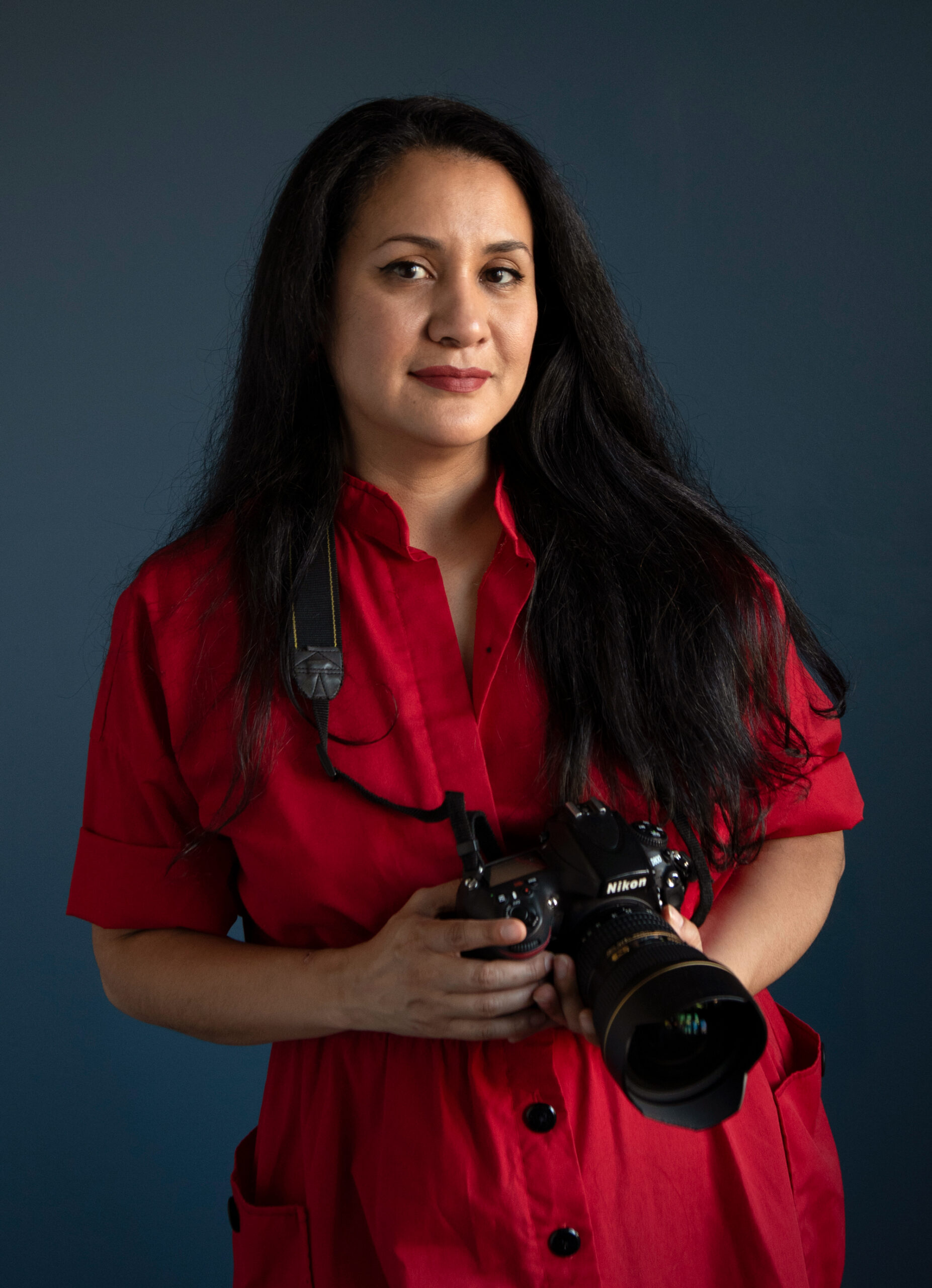 female photographer in red dress with long black hair holding a Nikon Camera